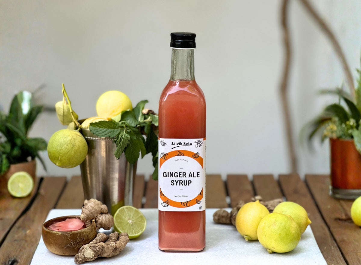 Bottle of Jaivik Setu ginger ale syrup on a table with lemons and ginger roots. Main image